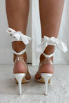 Close-up of elegant white high-heeled sandals featuring rhinestone bow embellishments and ankle-tie straps, perfect for weddings, parties, or special occasions.